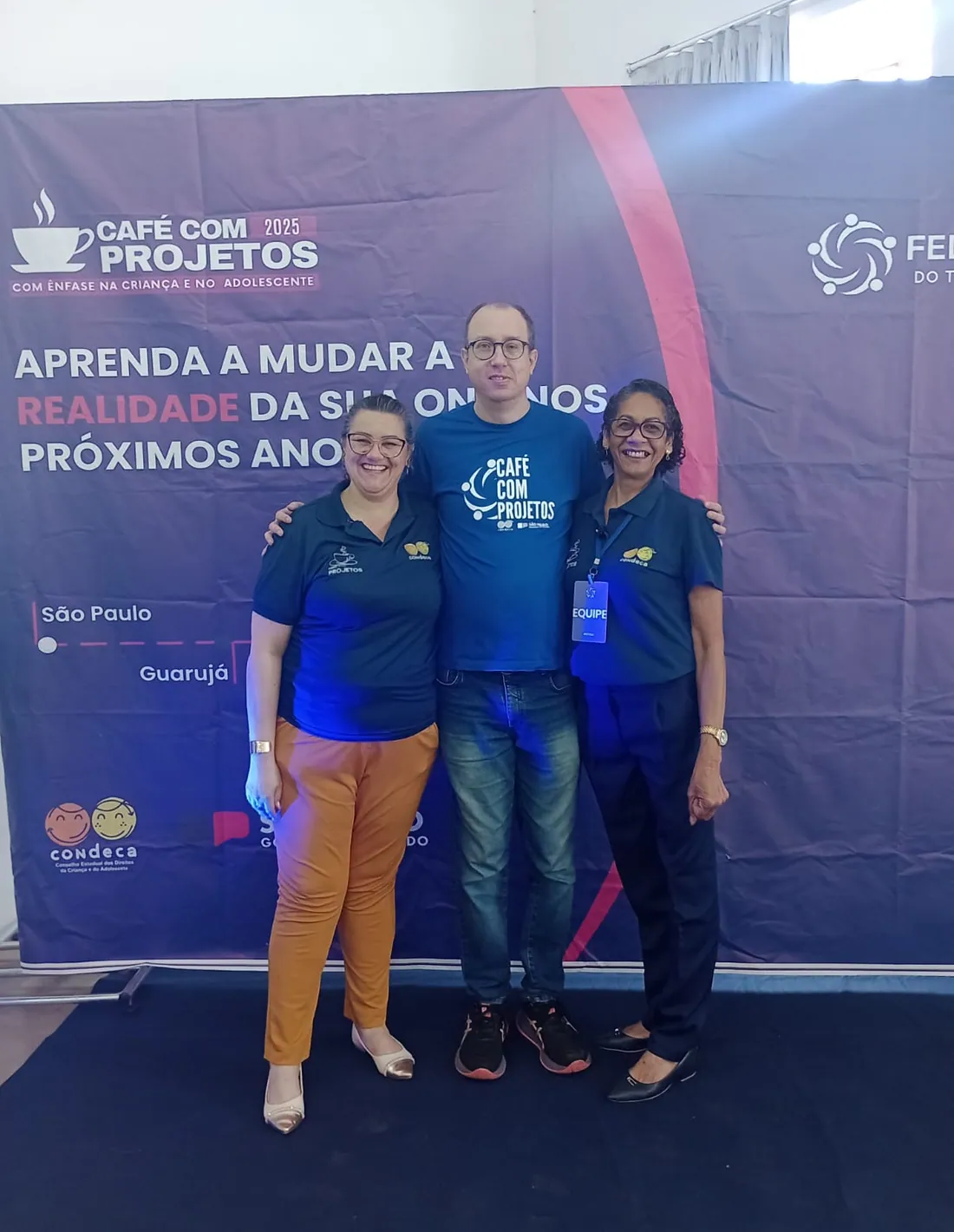 Equipe do Café com Projetos diante do painel do evento